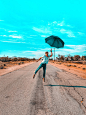 woman in teal long sleeve shirt and blue denim jeans holding umbrella walking on road during