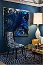 paint colors for living room, dark blue walls, blue and cream carpet, lighter blue and cream chair with black details, white lamp and glass table with gold details, large dark blue abstract painting