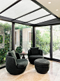 Inviting indoor-outdoor living space with plush black seating, glass walls, and lush greenery.