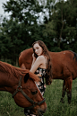 A young woman standing between two chestnut horses