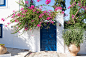 典型的希腊白色建筑的正面，蓝色的门和盛开的九重葛