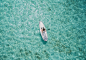 A drone shot of a woman paddling on a white wakeboard on the clear surface of water