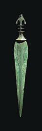 A LURISTAN BRONZE SWORD   CIRCA 9TH-7TH CENTURY B.C.   The tapering blade modelled with three ribs, each splitting in two towards the hilt, the waisted elliptical guard surmounted by two discs, the crescentic bifurcated pommel with notched finials  22 in.