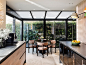 Modern kitchen-dining area with sleek black steel frame, natural wood cabinetry, and lush greenery views.