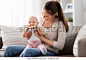 family, motherhood and people concept - happy smiling mother and little baby playing with teething toy or rattle at home
