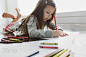 Little girl lying on floor coloring at home by Hero Images 