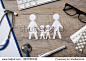 Top view of family paper chain on a doctor desk. Medical worktable with keyboard, blue stethoscope, pills and eyeglasses. Family healthcare, medicine and insurance concept.