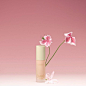 Against a pink blush background, a still life shows Éternité de Beauté foundation with two pink blooming flowers behind it.