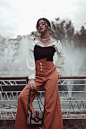 Photo of Woman in Black and White Top and Brown Trousers Posing While Leaning on Metal Railing  With Her Eyes Closed