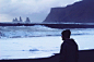 Man in a cap looking at the rough ocean on the rocky coastline at Vik