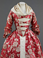 This 1760s gown features a rose-red silk with trails of ivory flowers woven in a complex technique. The gros de tours silk, dates from the 1740s, but the gown was been remade into the style of the 1760s. It may have started out as a fashionable 1740s sack