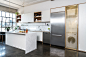 onewall kitchen with island and stacked washerdryer behind perforated brass door