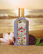 With the sun setting on the sea in the background, a bottle of the purple Gucci Flora Gorgeous Magnolia stands in sand with a pink Magnolia Alba flower on one side and dewberries on the other, to reflect its fresh and juicy ingredients.