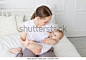 happy mom holds baby in her arms with a rodent in her mouth on a white bed with cotton bedding at home