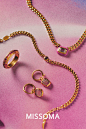 This may contain: three gold jewelry pieces on a pink background with the words missoma written below them