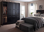 宽大的卧室内有一张黑色的床和床边桌，搭配着一个高大的黑色衣柜和两个带有灰色外套的脚凳。