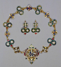 The necklace’s chain of snakes and crosses is gold enameled opaque white, pale-blue, light-green and translucent blue and green, set with pearls, rubies, and emeralds.  The earrings are also of enameled gold, set with pearls, and rubies. Made in the 16th 