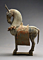 Terracotta horse statue, done in the Bei Wei style, is standing in a majestic pose with all four legs on the square-shaped base, with an elaborate saddle on its back: 