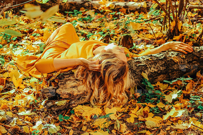 年轻美丽的女孩穿着黄色的长裙，躺在秋天公...
