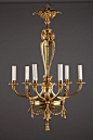 A beautiful Louis XVI style gilded bronze chandelier with six lights distributed by groups of two around a tripartite vertical scrolled structure, surmounted by three putti heads. The upper