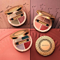 Four round clamshell compacts, three of them with their antiqued gold colored lids open to reveal three different eyeshadow shade combinations, are arranged casually on a surface covered in pressed powder, embossed with a portion of a sun pattern with sta