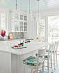 White shaker full- overlay cabinets, stacked uppers with divided light glass, planked ceiling (repeated on the back of the island), glass tile splash, satin nickel hardware, farm sink, countertop is granite or quartz (unclear in photo) with ogee edge. Cro