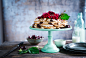 A cake stand with a cream cake covered in red flowers and cherries on a wooden table