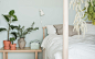 特写：床上配有浅色天然纺织品，映衬着浅绿色的墙壁，一张较低的白蜡木床边桌上放着植物和储物盒