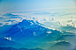 A bird's-eye view on a snow-capped mountain range with clouds obscuring the horizon