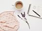 A bunch of lavender flowers next to a cup of coffee and a notepad on a white surface