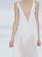 Long white pleated dress with staggered neckline; architectural fashion details // Akris