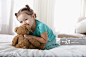 Hispanic girl hugging teddy bear on bed