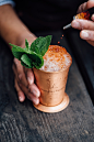 A person adding droplets of a brown liquid to a cocktail with ice