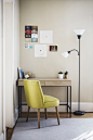 A small desk in the corner of a cozy room with a chair and a floor lamp