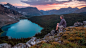 A man in a hat sitting on rocks overlooking a mountain lake