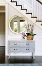 Console table under white staircase with round mirror and orchids