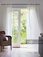 Rattan armchair next to lattice window with airy, white curtains and garden view