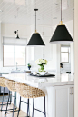 BECKI OWENS- Estillo Project: Classic Modern Kitchen. A white kitchen with statuary marble, Benjamin Moore Swiss Coffee paint, Rejuvenation swing arm sconce and black Butte cone pendants, Palecek rattan counter stools, island prep sink, and stainless stee