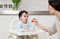 Mother feeding baby son in high chair