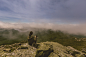 Girl with her dog sitting on rock and looking at mountains