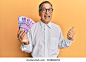 Middle age indian man holding 100 philippine peso banknotes pointing thumb up to the side smiling happy with open mouth  库存照片
