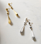 A color photo shows two pairs of David Yurman women’s earrings from the Renaissance Collection scattered on a grey marble surface nearby a white-and-pink flower, a perfume bottle and a golden tray. One pair is crafted from 18K yellow gold and the other pa