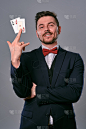 身穿黑色经典套装和红色领结的男子在灰色演播室背景下展示两张扑克牌。赌博、扑克、赌场。特写镜头