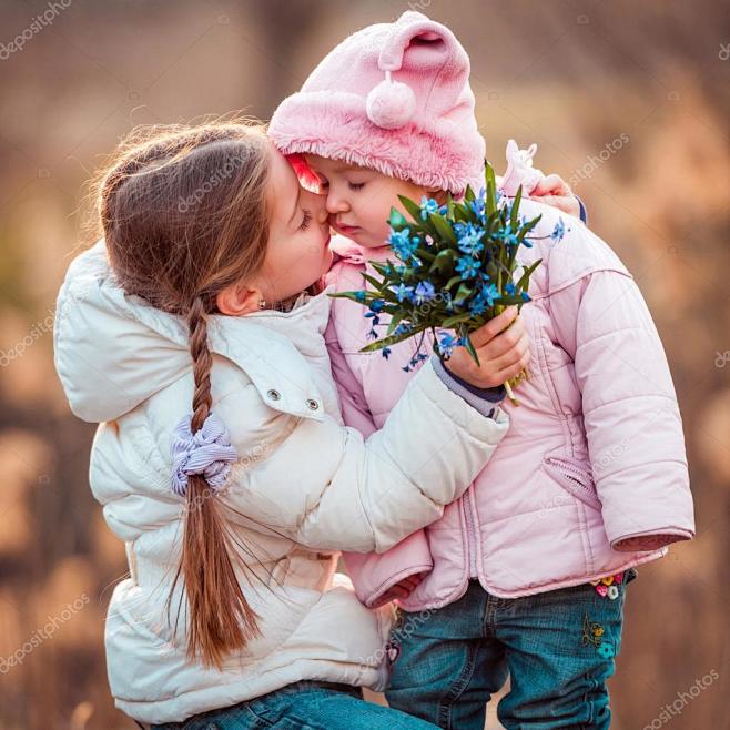 快乐的小女孩，亲吻她的妹妹和抱着雪花莲一...