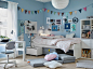 蓝色墙壁的青少年卧室中摆放着一张 SLÄKT 斯莱克 白色床，物品放在床底，旁边是 PÅHL 佩尔 书桌和 ÖRFJÄLL 奥菲 白色和灰色少年书桌椅。