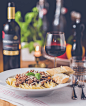 A plate with a pasta dish next to a wine bottle and a glass of red wine on a set table