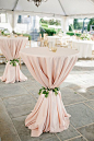 Don’t just drape your cocktail tables in linen and call it a day; cinch it with a tie of lush greenery — or twine or fabric if you wish — to give a little pizazz to its silhouette.: 