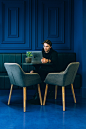 A man looking at a laptop on a leather seat at a blue wall