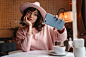 其中包括图片：Woman indoors in cafe using mobile phone take a selfie.