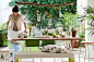 View of casually laid wooden dining table with plants and green accessories. Customised wooden NORNAS bench with botanical print cushions.